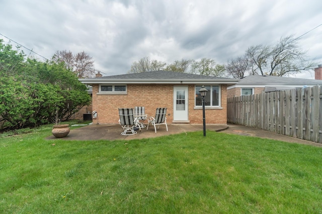 back of house with a chimney, fence, brick siding, a yard, and a patio