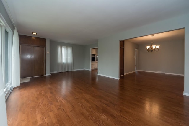 unfurnished living room featuring dark wood-style floors, baseboards, and an inviting chandelier