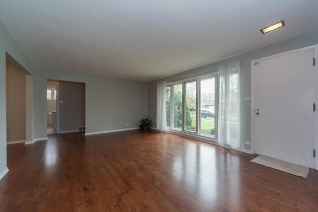unfurnished living room featuring visible vents, baseboards, dark wood-style flooring, and a healthy amount of sunlight