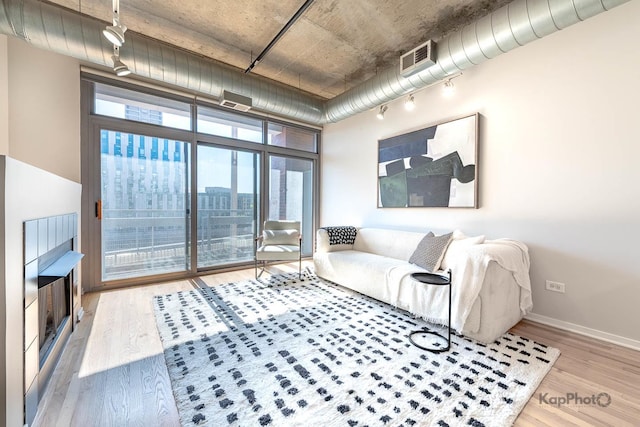 living room with floor to ceiling windows, wood finished floors, rail lighting, visible vents, and baseboards