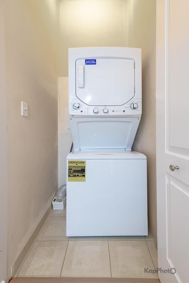 washroom with baseboards, stacked washer and clothes dryer, laundry area, and light tile patterned floors