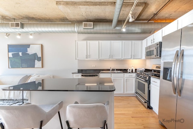 kitchen with dark countertops, a breakfast bar area, stainless steel appliances, white cabinets, and visible vents