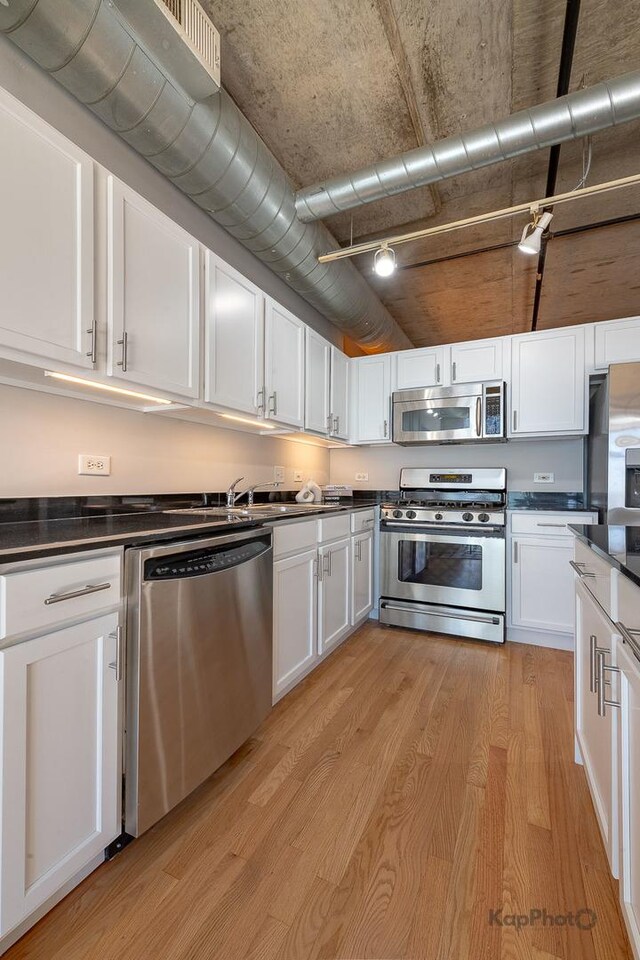 kitchen featuring dark countertops, white cabinetry, stainless steel appliances, and light wood finished floors