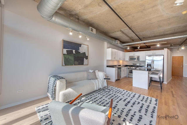 living area with visible vents, light wood-style flooring, baseboards, and rail lighting