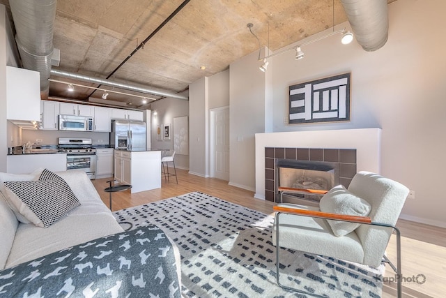 living area with a tiled fireplace, light wood finished floors, and baseboards