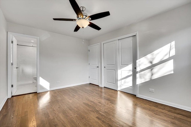 unfurnished bedroom with baseboards, a ceiling fan, wood finished floors, a closet, and connected bathroom