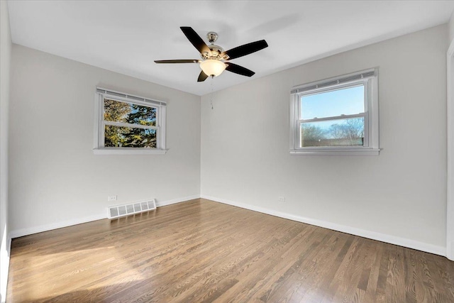 empty room with baseboards, wood finished floors, visible vents, and a wealth of natural light