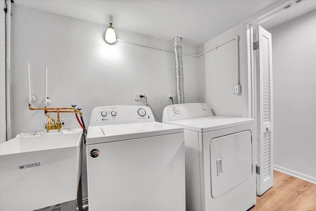 clothes washing area with washing machine and clothes dryer, a sink, light wood-type flooring, baseboards, and laundry area