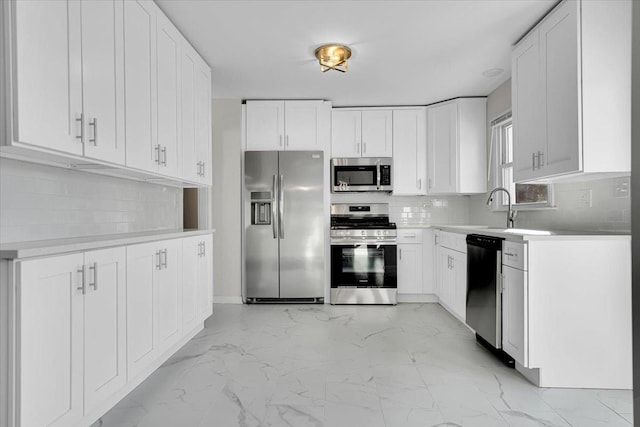 kitchen featuring marble finish floor, stainless steel appliances, light countertops, a sink, and decorative backsplash