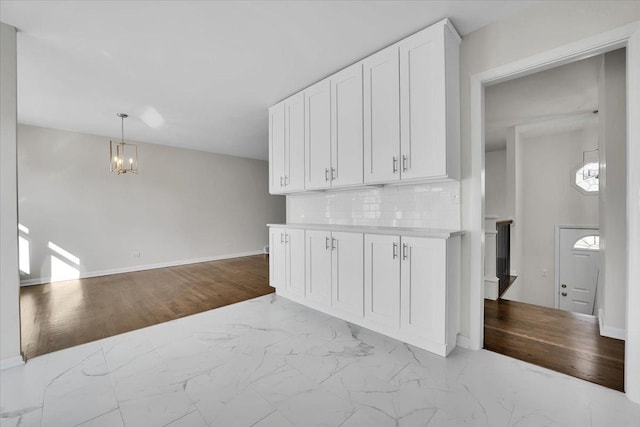 interior space featuring marble finish floor, an inviting chandelier, white cabinetry, and tasteful backsplash