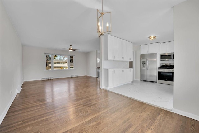 unfurnished living room featuring light wood-type flooring, baseboards, visible vents, and ceiling fan with notable chandelier