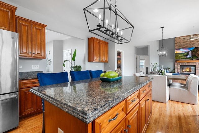 kitchen with a brick fireplace, light wood-style flooring, a center island, freestanding refrigerator, and open floor plan