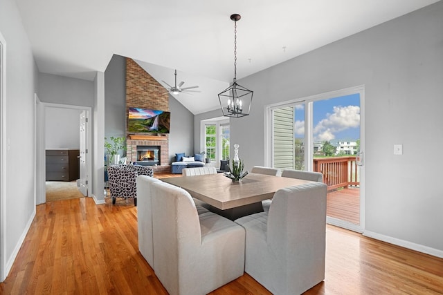 dining room with light wood-style floors, baseboards, a fireplace, and vaulted ceiling