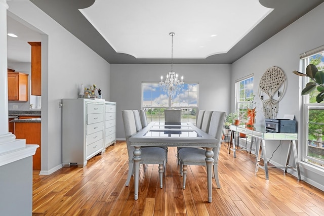 dining area with light wood-type flooring, a raised ceiling, baseboards, and a notable chandelier