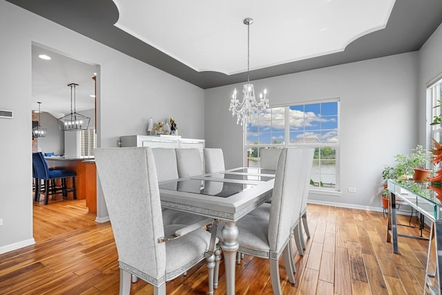 dining room with a notable chandelier, hardwood / wood-style floors, baseboards, a tray ceiling, and visible vents