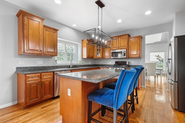 kitchen with appliances with stainless steel finishes, light wood-type flooring, brown cabinets, an inviting chandelier, and a breakfast bar