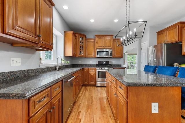 kitchen with brown cabinets, appliances with stainless steel finishes, a sink, light wood-style flooring, and a kitchen island