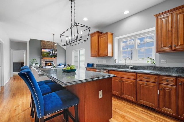 kitchen featuring a kitchen island, a kitchen bar, a fireplace, a sink, and light wood finished floors