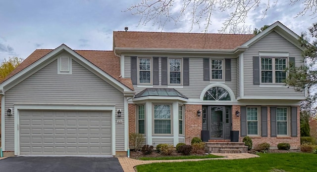 view of front of home with roof with shingles, brick siding, aphalt driveway, and a front lawn