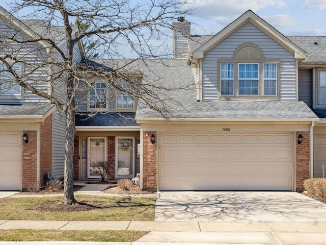 traditional-style home with concrete driveway, a chimney, a shingled roof, an attached garage, and brick siding