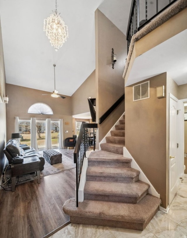 stairway featuring visible vents, high vaulted ceiling, and ceiling fan with notable chandelier