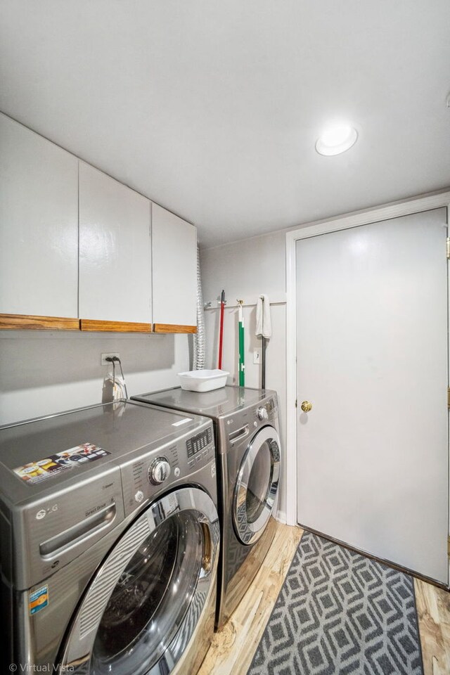 washroom featuring cabinet space, washing machine and clothes dryer, and light wood-type flooring