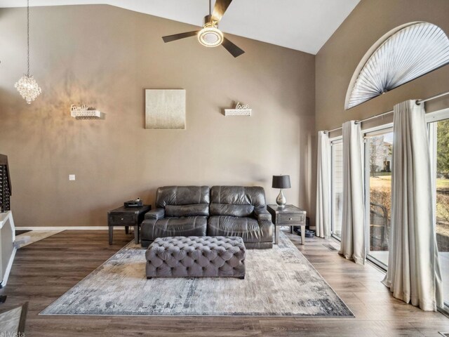 living area featuring high vaulted ceiling, baseboards, wood finished floors, and ceiling fan with notable chandelier