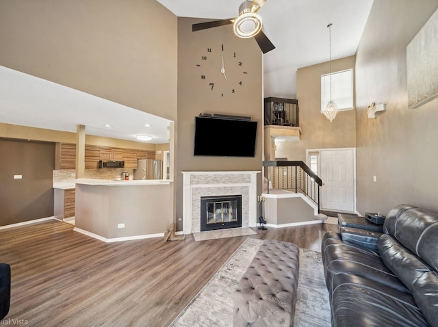 living area with baseboards, wood finished floors, ceiling fan with notable chandelier, and a high ceiling