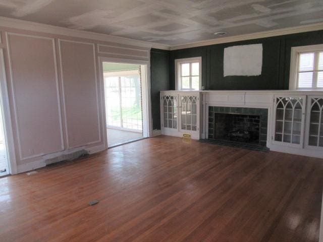 unfurnished living room with wood finished floors, ornamental molding, a decorative wall, and a fireplace