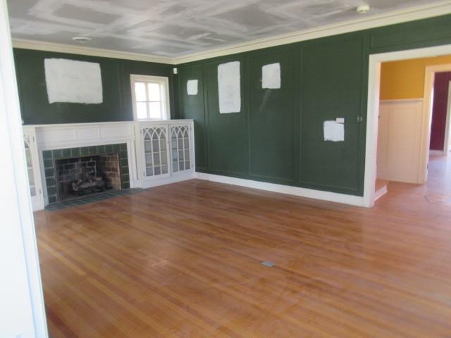 unfurnished living room featuring wood finished floors, ornamental molding, a decorative wall, and a fireplace