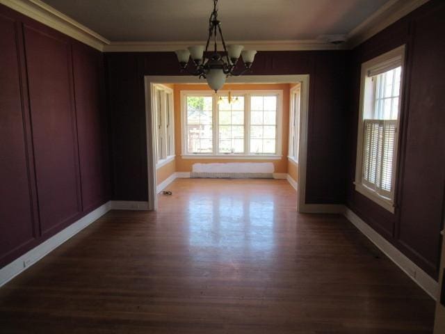 unfurnished dining area featuring crown molding, baseboards, a notable chandelier, and dark wood-style floors