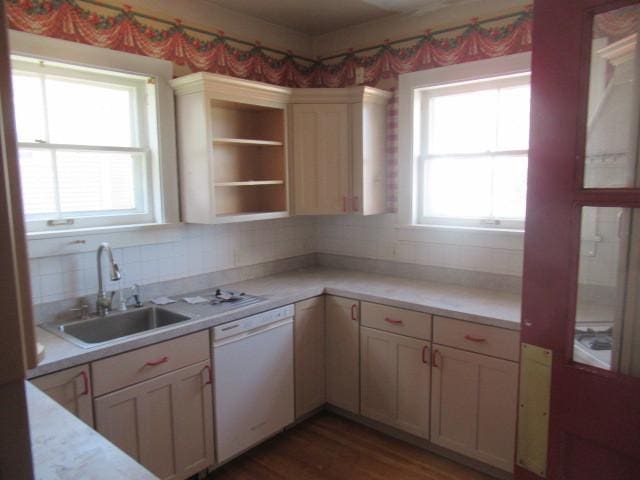 kitchen featuring a sink, dishwasher, light countertops, decorative backsplash, and wood finished floors