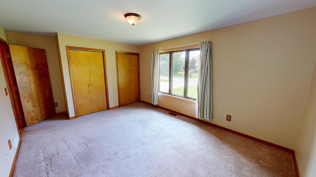 unfurnished bedroom featuring two closets, baseboards, visible vents, and carpet floors