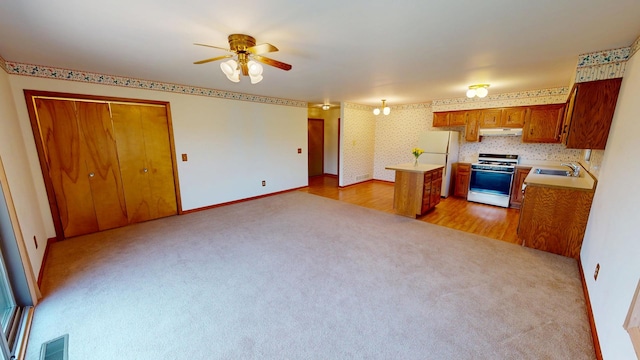 kitchen featuring a sink, gas stove, brown cabinetry, under cabinet range hood, and visible vents