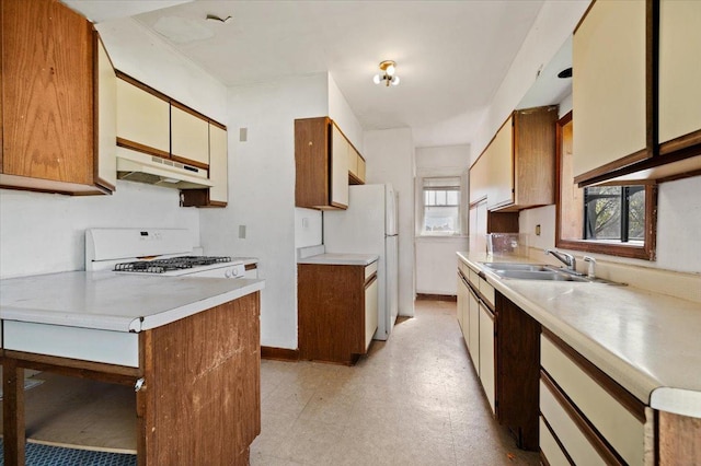 kitchen with a sink, under cabinet range hood, white appliances, light countertops, and light floors