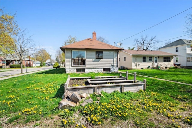 back of property featuring a chimney, a yard, and a garden