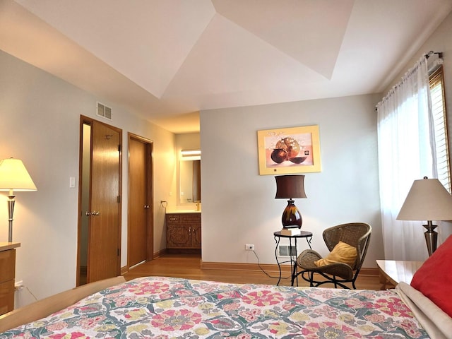bedroom featuring visible vents, lofted ceiling, light wood-style floors, baseboards, and connected bathroom
