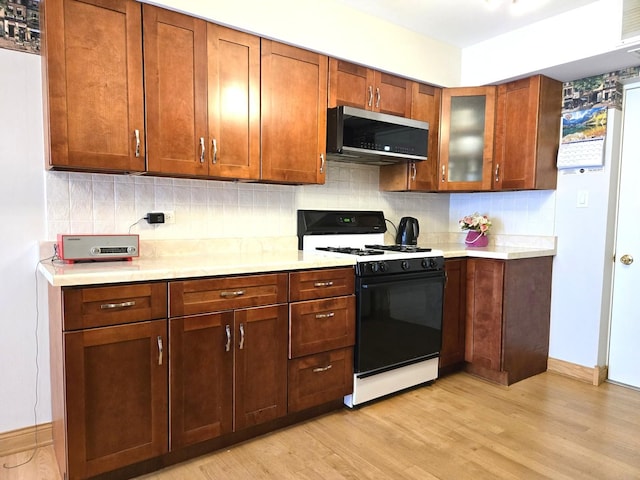 kitchen with light countertops, stainless steel microwave, light wood finished floors, backsplash, and gas stove
