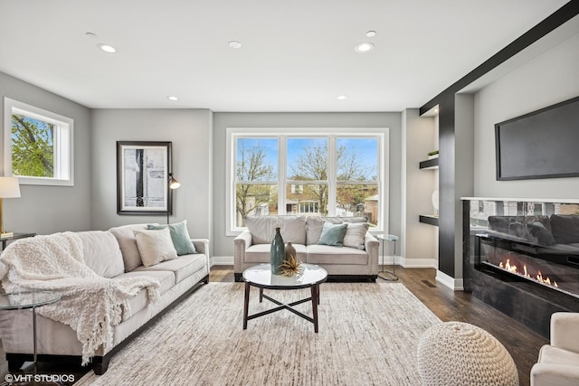 living room featuring baseboards, a glass covered fireplace, recessed lighting, and wood finished floors