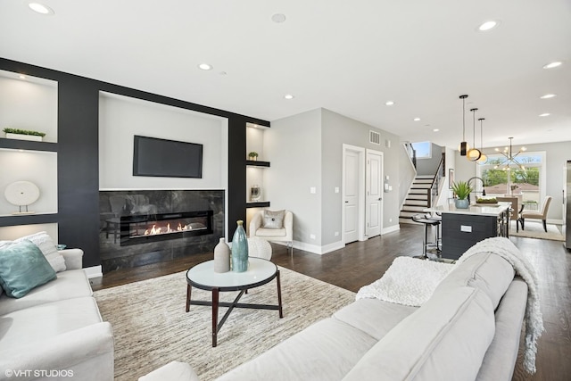 living area featuring stairway, baseboards, dark wood-style floors, a glass covered fireplace, and recessed lighting