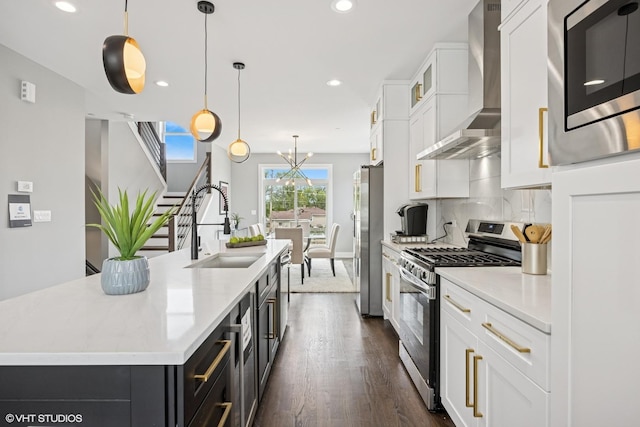 kitchen with a sink, wall chimney range hood, a kitchen island with sink, light countertops, and appliances with stainless steel finishes