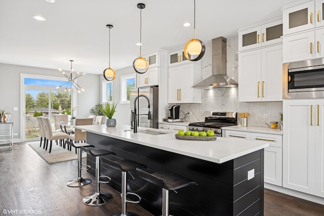 kitchen featuring a sink, stainless steel appliances, wall chimney range hood, dark wood finished floors, and backsplash