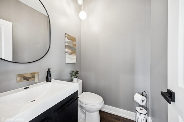 half bath with toilet, baseboards, vanity, and wood finished floors