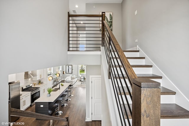staircase featuring wood finished floors, a towering ceiling, and recessed lighting
