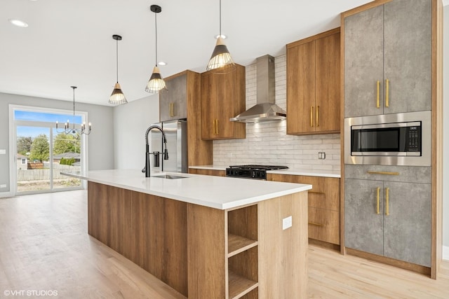 kitchen featuring wall chimney exhaust hood, brown cabinets, appliances with stainless steel finishes, and light wood-style flooring