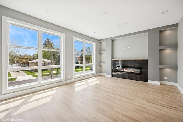unfurnished living room featuring baseboards, a glass covered fireplace, wood finished floors, and built in shelves