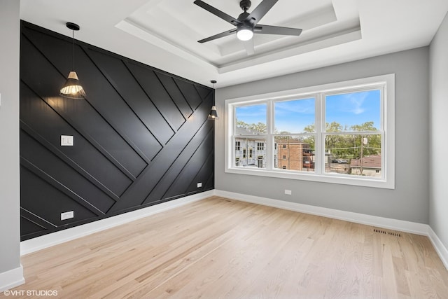 unfurnished room featuring visible vents, baseboards, a raised ceiling, ceiling fan, and light wood-style floors