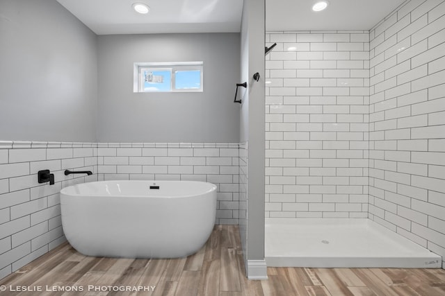 full bathroom with tile walls, recessed lighting, a freestanding tub, wood finished floors, and a shower stall