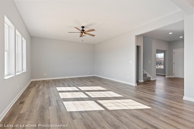 unfurnished living room featuring visible vents, baseboards, wood finished floors, stairs, and ceiling fan