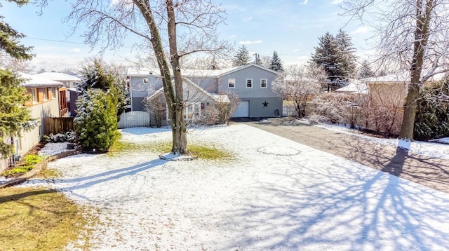 snowy yard with a residential view, an attached garage, gravel driveway, and fence